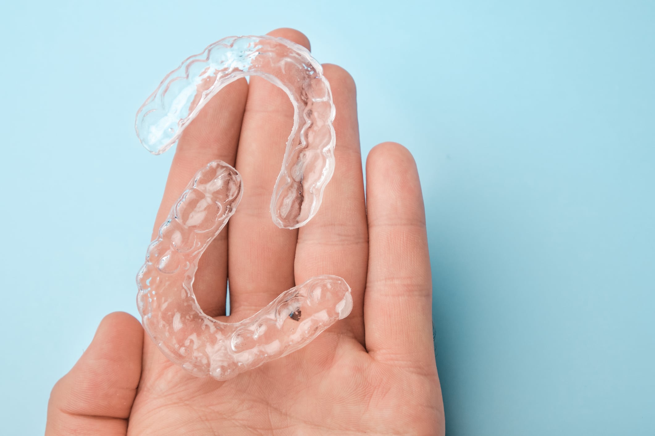 Close up mans hand holding invisible aligners for whitening and straightening of teeth on the blue background. Orthodontic therapy after brackets. Teeth healthcare.
