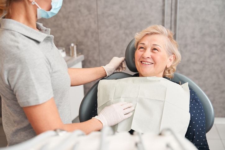 Portrait of smiling senior woman sitting in dental chair and listening to female dentist calming her and explaining something about treatment. People at the dentist office concept