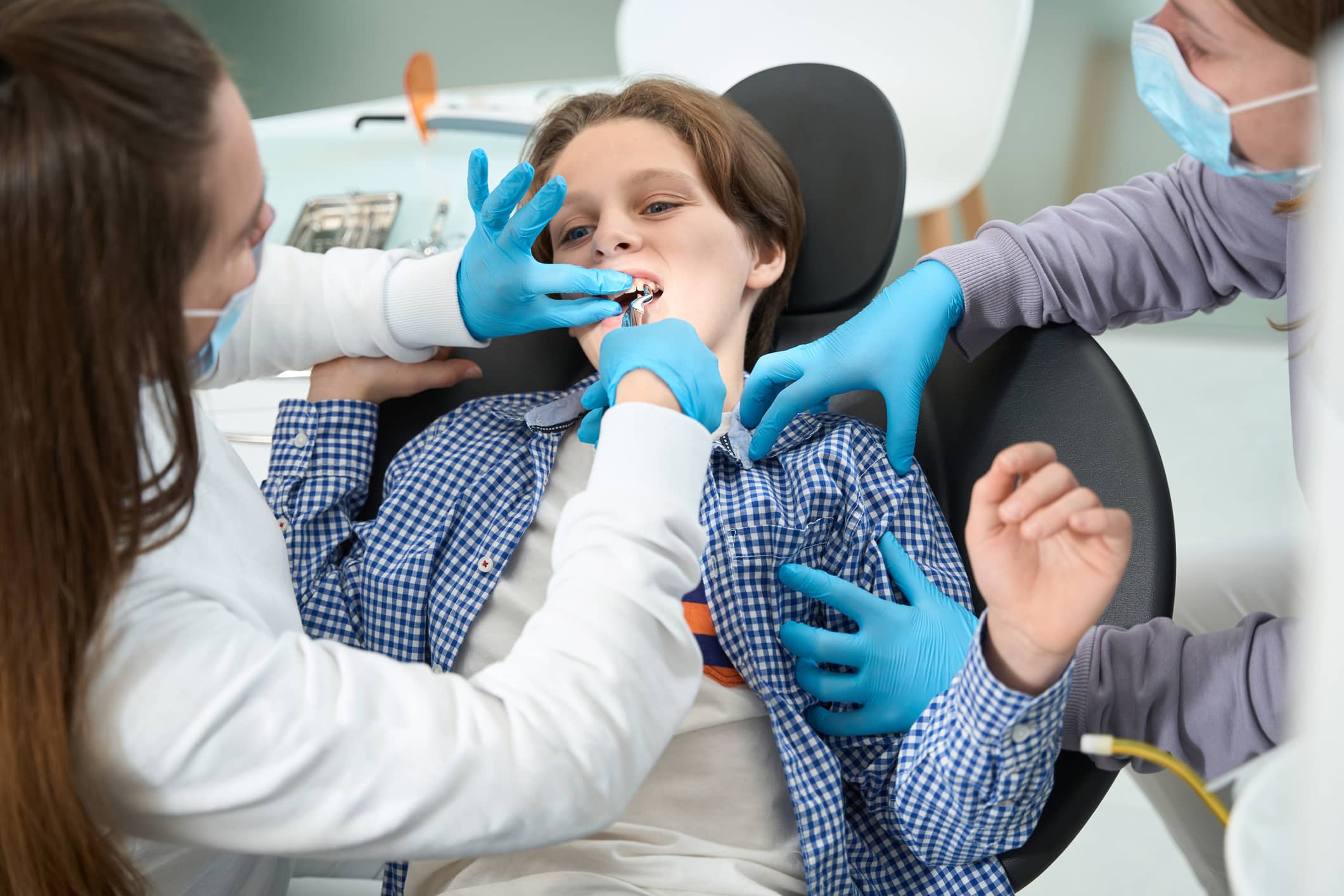 Dentist-surgeon removes a tooth to a teenager with a special tool, an assistant holds the boy